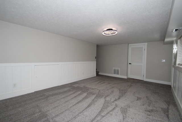 carpeted empty room featuring a wainscoted wall, visible vents, and a textured ceiling