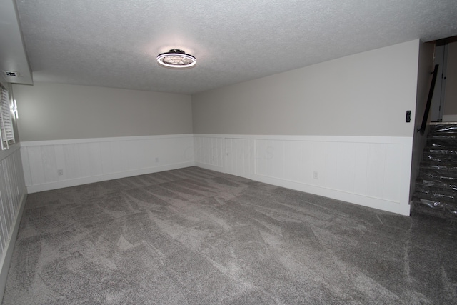 carpeted spare room with a textured ceiling and wainscoting