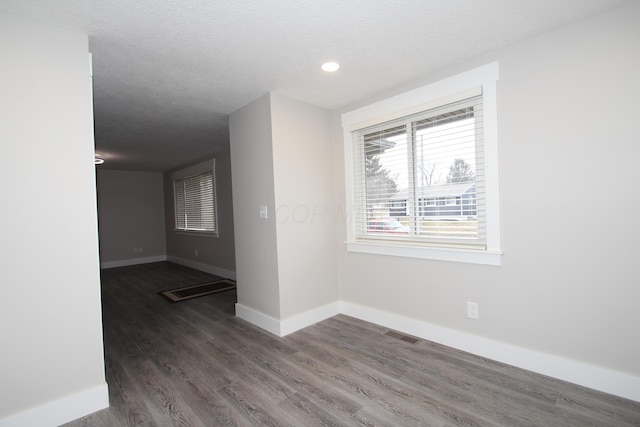 empty room with visible vents, a textured ceiling, baseboards, and wood finished floors