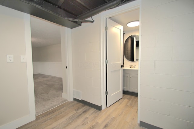 corridor featuring light wood-type flooring, visible vents, a sink, and concrete block wall