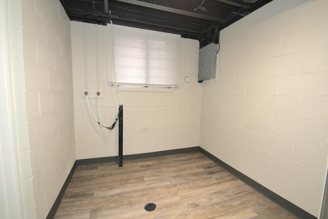 unfinished below grade area with wood finished floors, electric panel, and concrete block wall