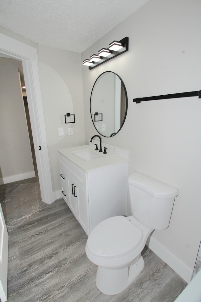 bathroom featuring toilet, vanity, a textured ceiling, wood finished floors, and baseboards