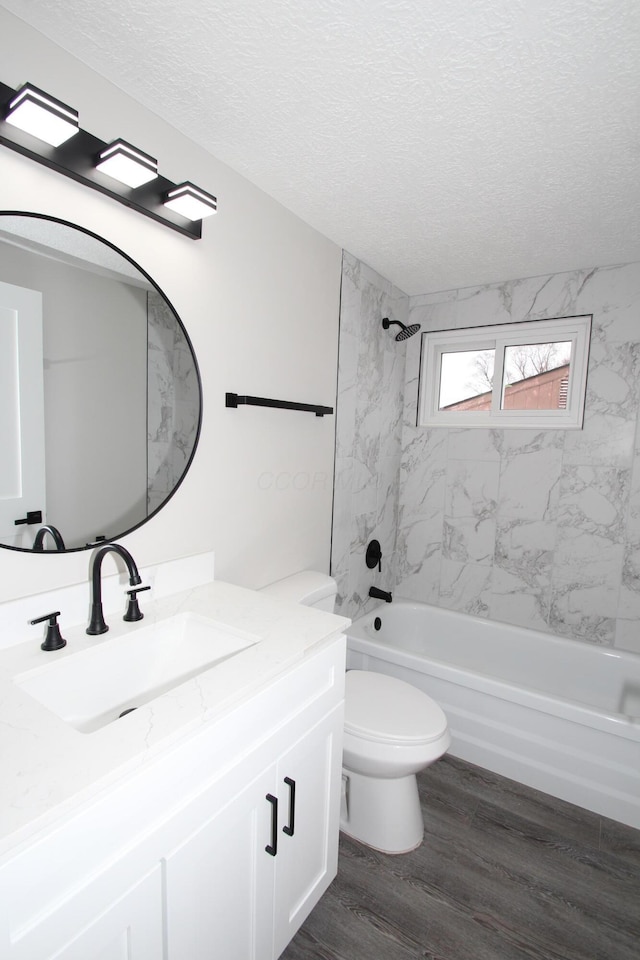 full bath featuring a textured ceiling, toilet, wood finished floors, vanity, and shower / washtub combination