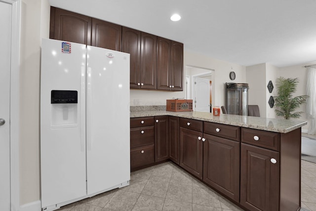 kitchen featuring a peninsula, light stone countertops, white fridge with ice dispenser, and dark brown cabinets