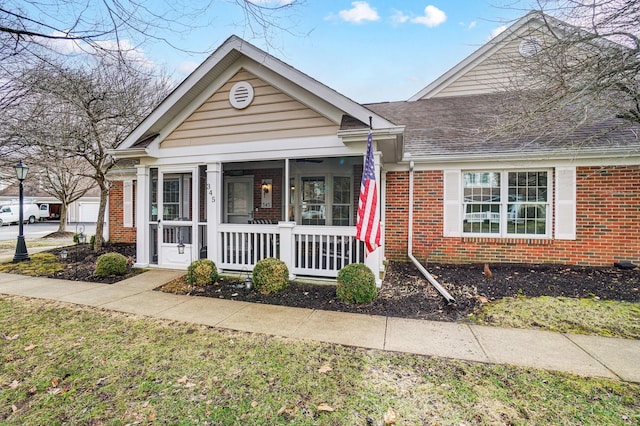 view of front of home featuring covered porch, a shingled roof, and brick siding