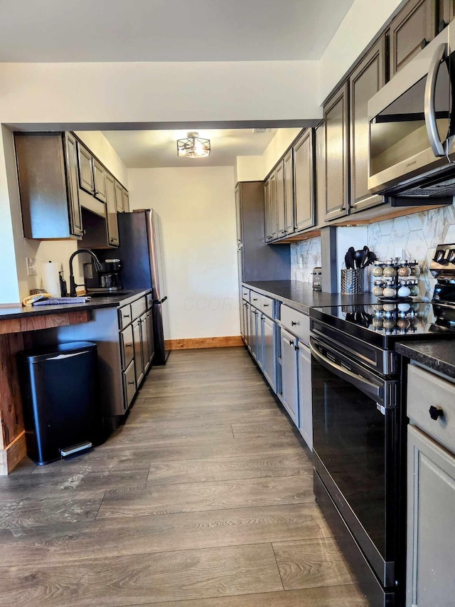 kitchen with tasteful backsplash, dark countertops, stainless steel microwave, dark wood-style flooring, and black range with electric stovetop