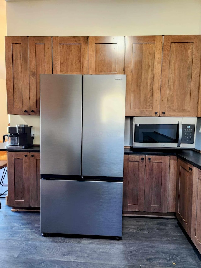 kitchen featuring dark countertops, brown cabinetry, appliances with stainless steel finishes, and dark wood finished floors