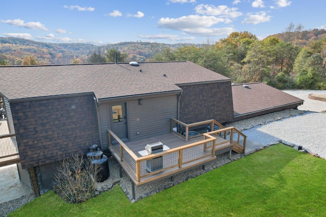 rear view of property with roof with shingles, a yard, a view of trees, and a wooden deck