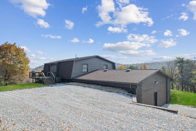 back of house featuring central AC, a shingled roof, a wooden deck, and a gambrel roof