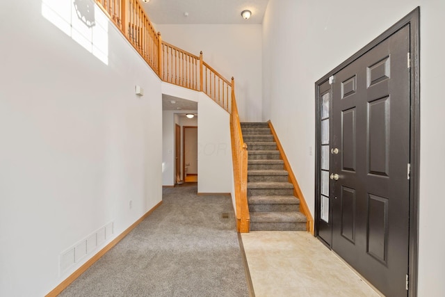 carpeted entrance foyer with stairs, a high ceiling, visible vents, and baseboards