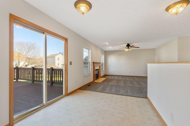 unfurnished living room featuring a fireplace with flush hearth, light carpet, ceiling fan, a textured ceiling, and baseboards