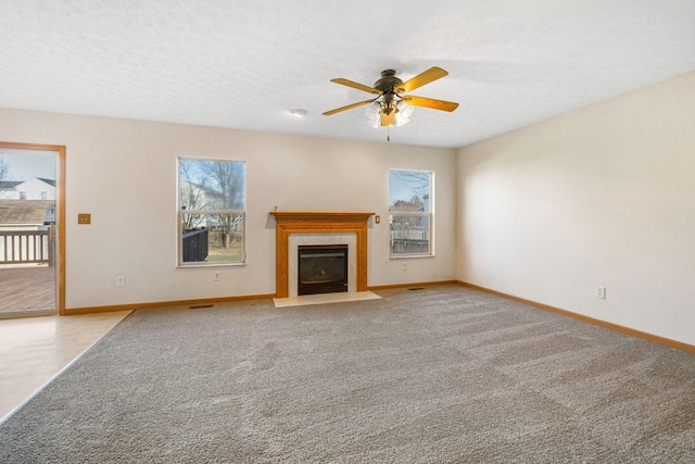 unfurnished living room with a fireplace with flush hearth, ceiling fan, a textured ceiling, and baseboards