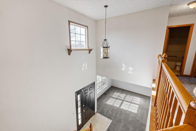 hall with a textured ceiling, carpet floors, and an upstairs landing