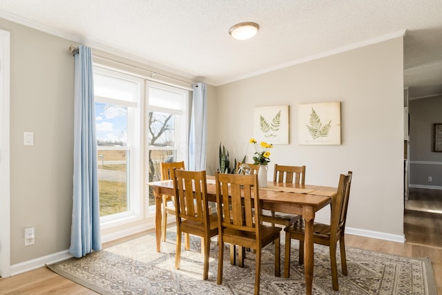 dining space with light wood-type flooring, baseboards, a textured ceiling, and crown molding