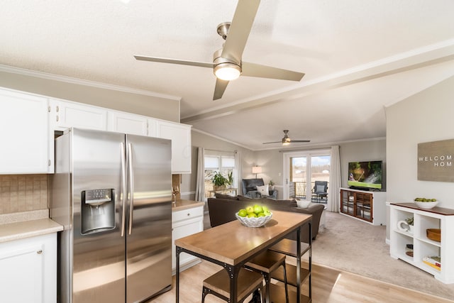 kitchen featuring crown molding, light countertops, vaulted ceiling, stainless steel refrigerator with ice dispenser, and white cabinets