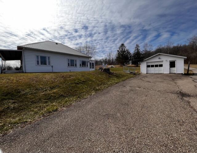 view of side of property with a detached garage, aphalt driveway, a lawn, and an outbuilding