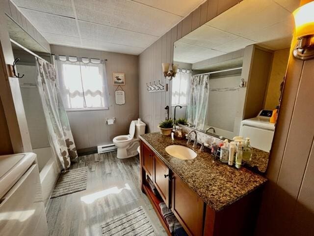 full bathroom featuring toilet, a baseboard heating unit, wood finished floors, vanity, and washer / dryer