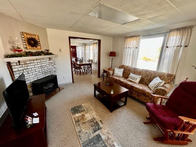 living area with a paneled ceiling, a brick fireplace, carpet, and a wealth of natural light