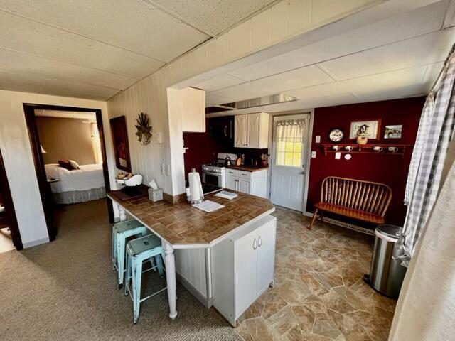 kitchen featuring stainless steel gas range, dark countertops, white cabinets, and light carpet