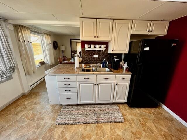 kitchen with a baseboard heating unit, a sink, freestanding refrigerator, and white cabinets