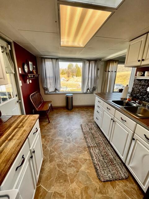 kitchen featuring a healthy amount of sunlight, butcher block countertops, white cabinets, and a sink