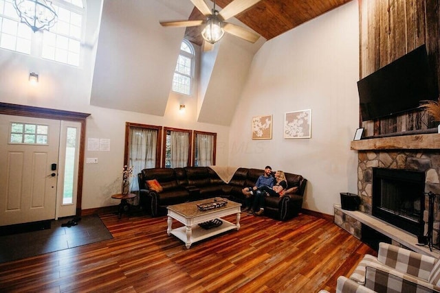 living room featuring dark wood-style floors, high vaulted ceiling, a stone fireplace, and baseboards