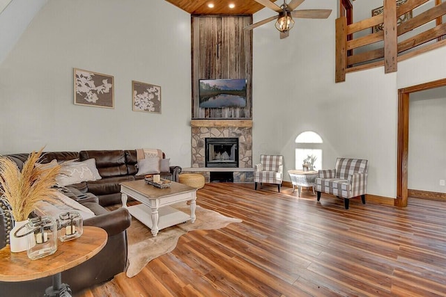 living room with a towering ceiling, baseboards, wood finished floors, and a stone fireplace