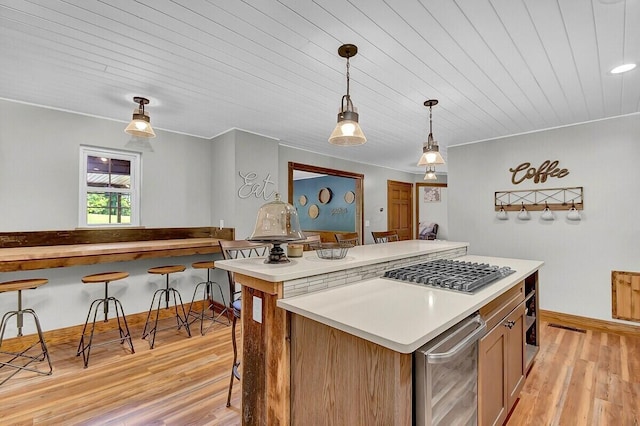 kitchen featuring light wood-style flooring, stainless steel gas cooktop, light countertops, a center island, and decorative light fixtures