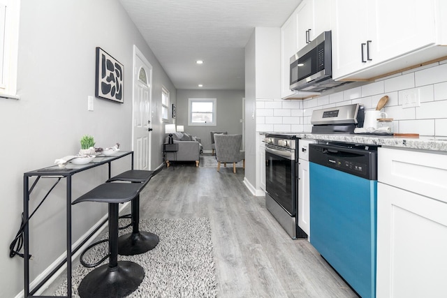 kitchen featuring baseboards, stainless steel appliances, light wood-style floors, white cabinetry, and backsplash