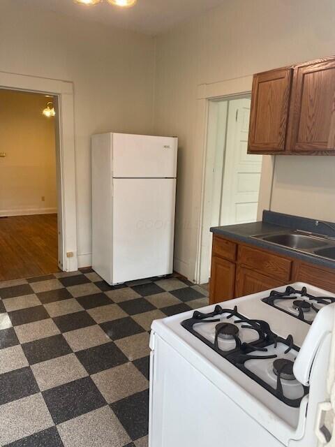 kitchen with white appliances, dark countertops, dark floors, brown cabinets, and a sink