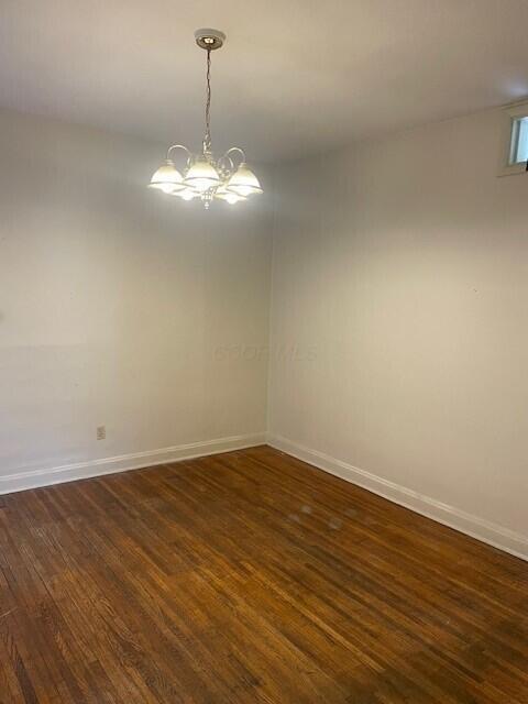 spare room featuring an inviting chandelier, baseboards, and dark wood finished floors