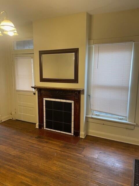 unfurnished living room featuring dark wood-type flooring, a tile fireplace, and baseboards