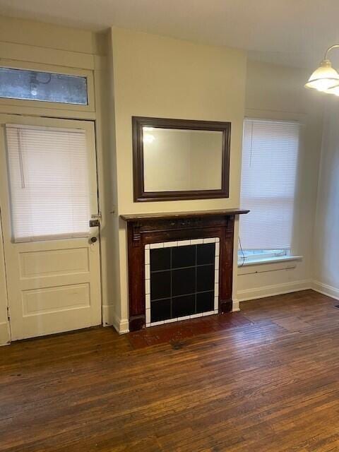 unfurnished living room featuring dark wood-style flooring, a tiled fireplace, and baseboards