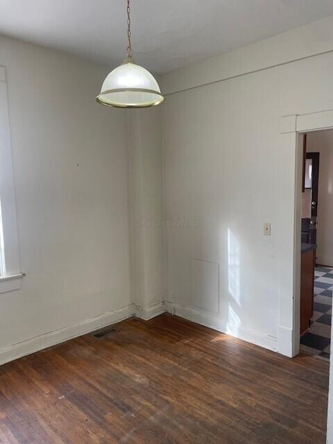 empty room with wood finished floors, visible vents, and baseboards