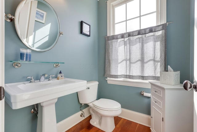 half bathroom featuring wood finished floors, toilet, and baseboards