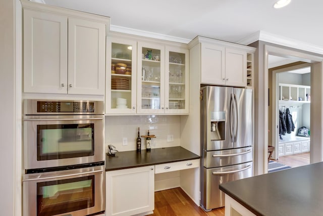 kitchen with tasteful backsplash, dark countertops, glass insert cabinets, stainless steel appliances, and white cabinetry