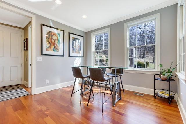 dining space featuring baseboards, visible vents, crown molding, and wood finished floors