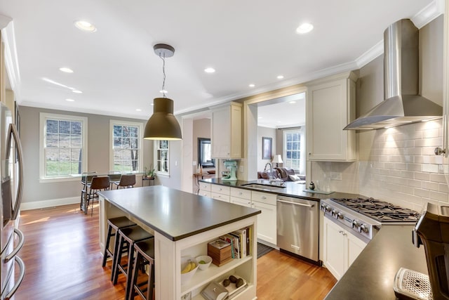 kitchen with dark countertops, ornamental molding, stainless steel appliances, wall chimney range hood, and a sink