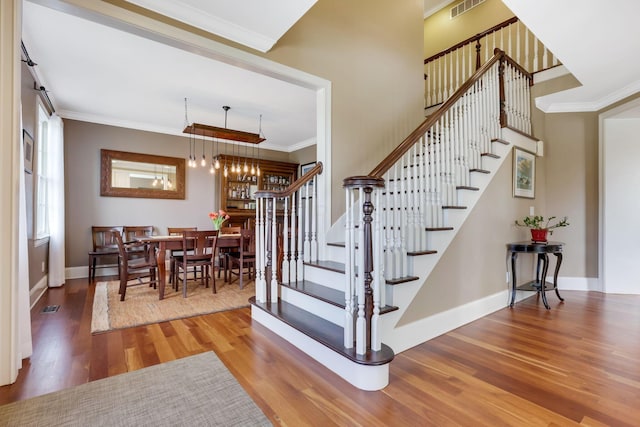 stairway with ornamental molding, a notable chandelier, baseboards, and wood finished floors