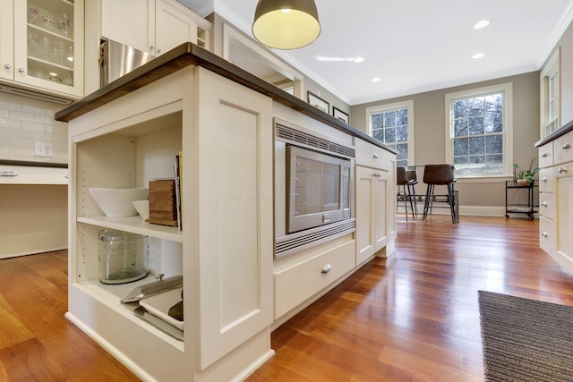 kitchen with tasteful backsplash, stainless steel microwave, crown molding, and glass insert cabinets