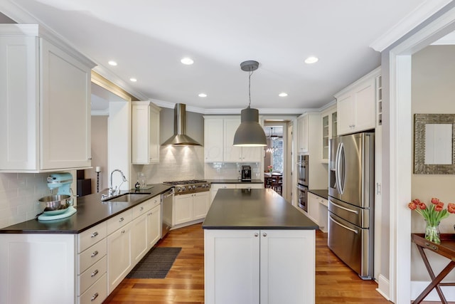 kitchen featuring dark countertops, wall chimney exhaust hood, light wood-style flooring, stainless steel appliances, and a sink