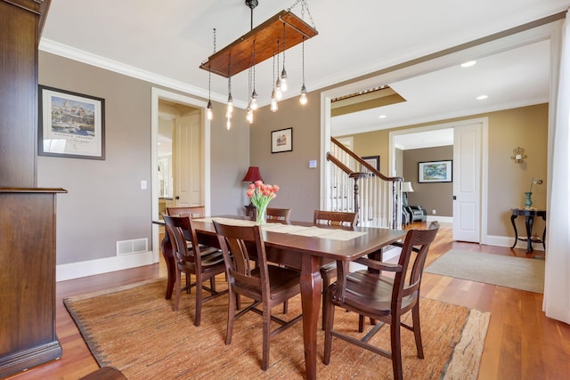 dining area with ornamental molding, light wood-style flooring, and visible vents