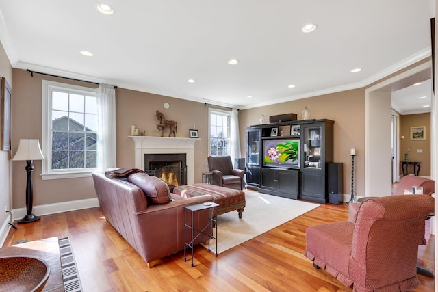 living area featuring recessed lighting, baseboards, a lit fireplace, light wood finished floors, and crown molding