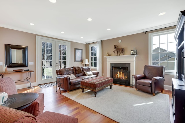 living area featuring a healthy amount of sunlight, a fireplace with flush hearth, ornamental molding, and french doors