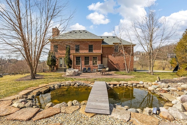 back of house featuring a chimney, brick siding, a small pond, and french doors