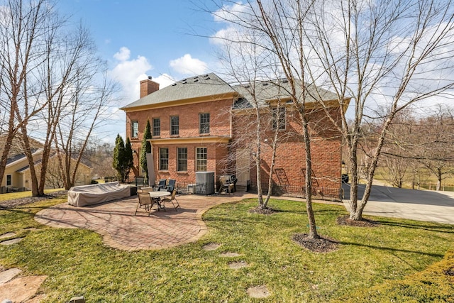 rear view of house featuring brick siding, a chimney, central air condition unit, a lawn, and a patio area