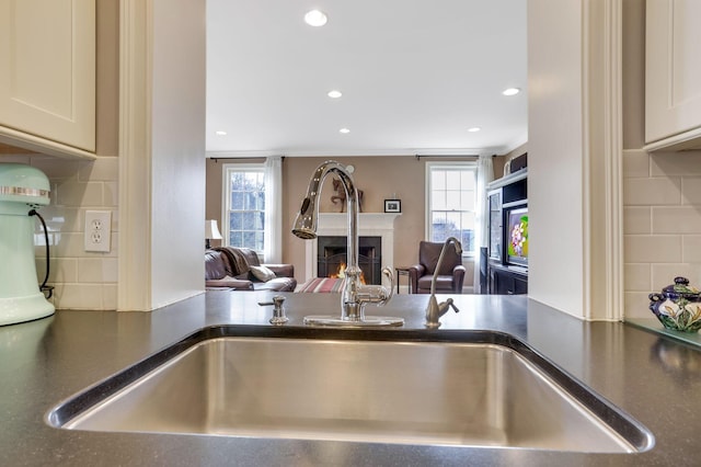 details featuring dark countertops, a sink, a lit fireplace, and decorative backsplash