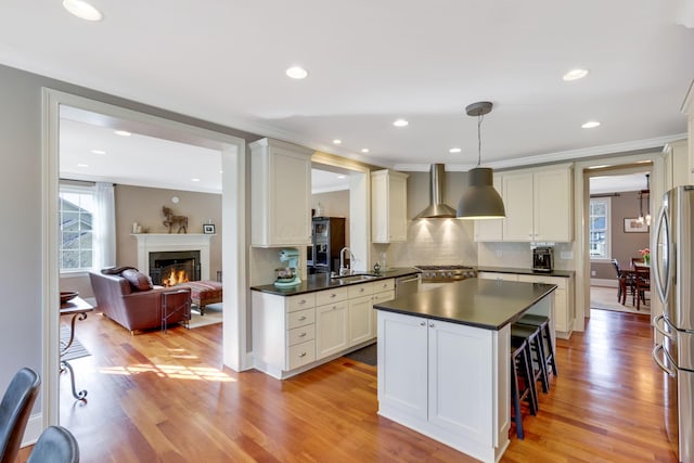 kitchen with dark countertops, light wood-style flooring, appliances with stainless steel finishes, wall chimney range hood, and a sink