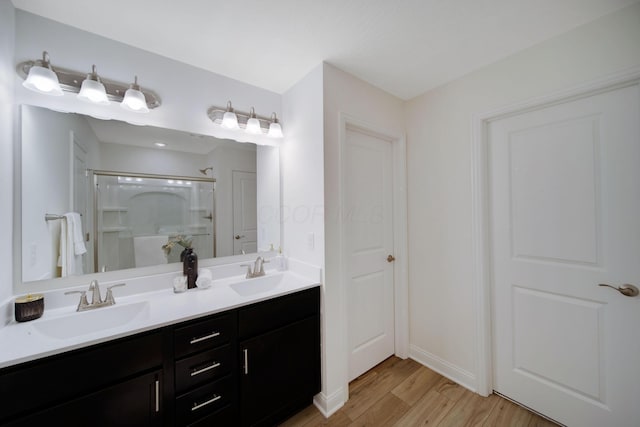 full bathroom featuring wood finished floors, a walk in shower, double vanity, and a sink