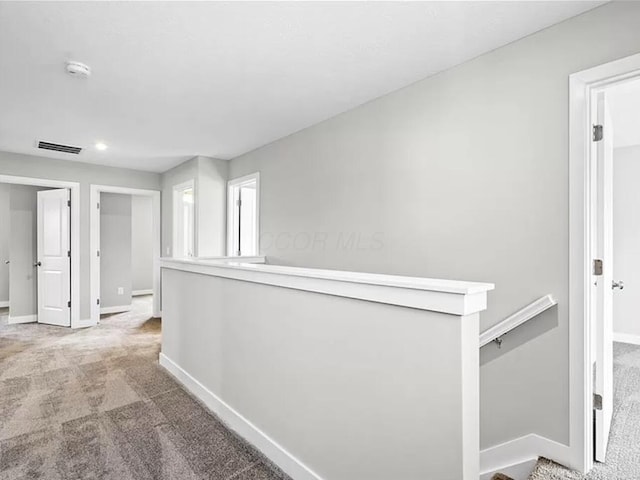 corridor featuring visible vents, an upstairs landing, baseboards, and carpet flooring